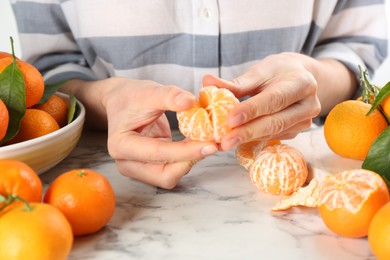 Woman peeling fresh ripe tangerine at white marble table, closeup