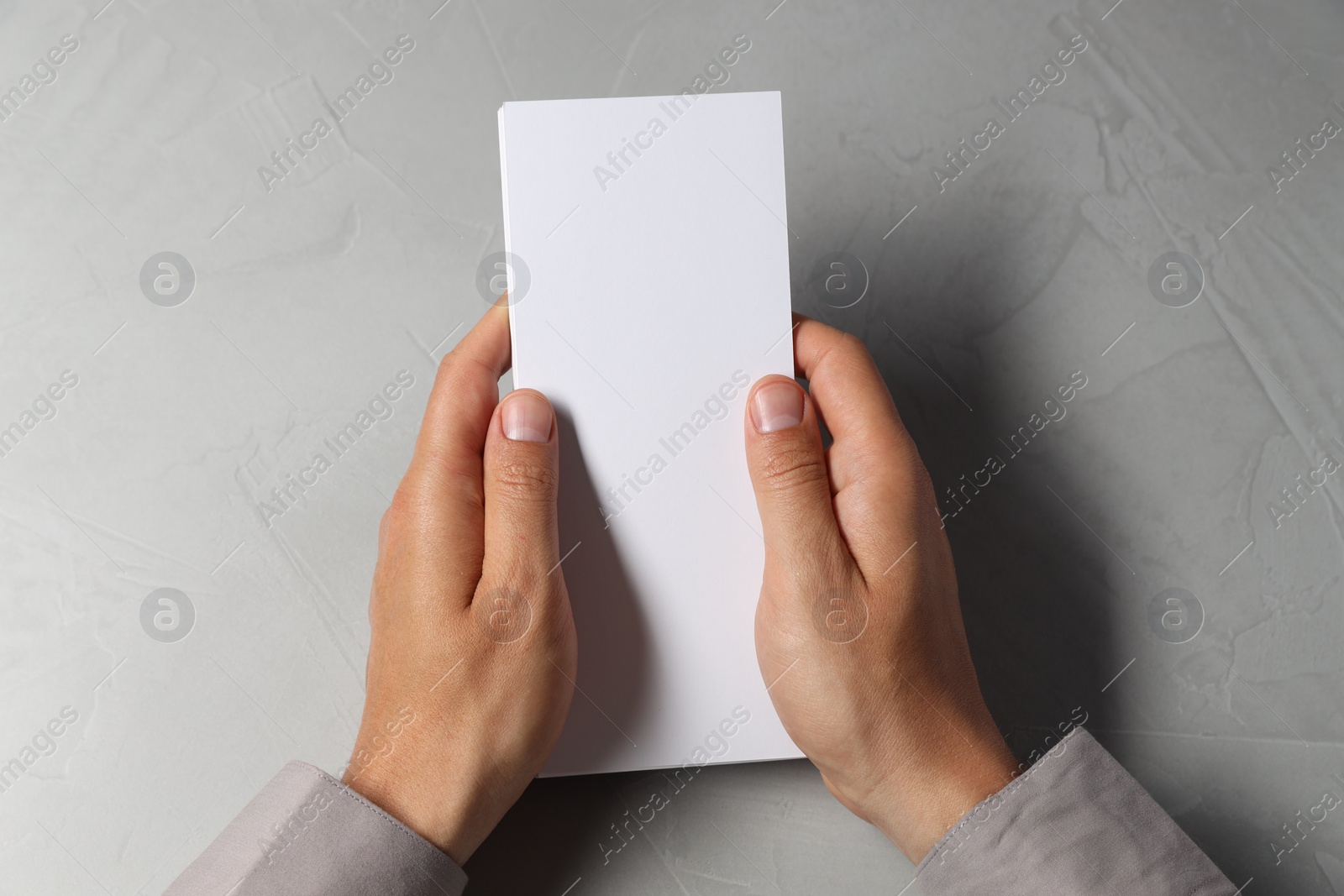 Photo of Man holding white blank card at light grey table, top view. Mockup for design
