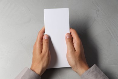 Photo of Man holding white blank card at light grey table, top view. Mockup for design