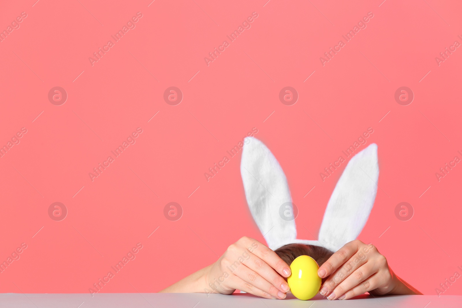 Photo of Little girl wearing bunny ears headband  and playing with Easter egg at table against color background, space for text