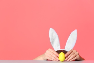 Photo of Little girl wearing bunny ears headband  and playing with Easter egg at table against color background, space for text