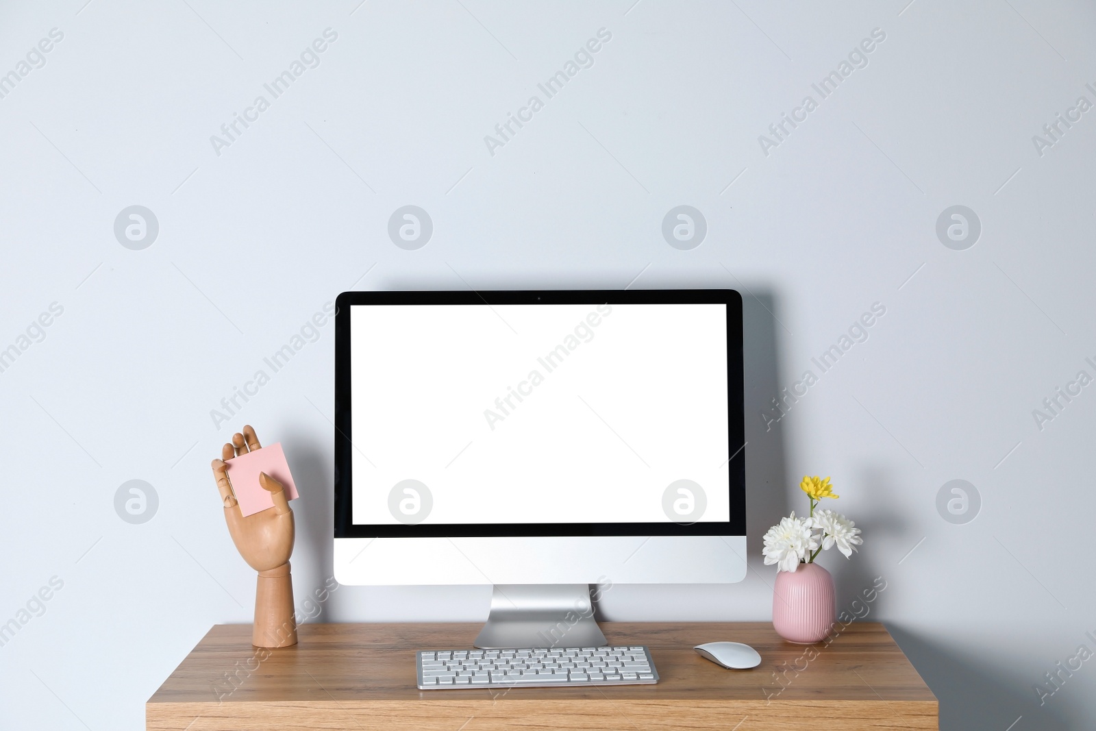 Photo of Modern computer monitor on desk against light wall, mock up with space for text