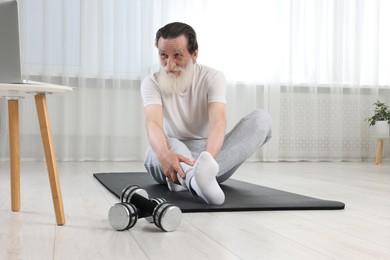 Photo of Senior man stretching on mat at home. Sports equipment