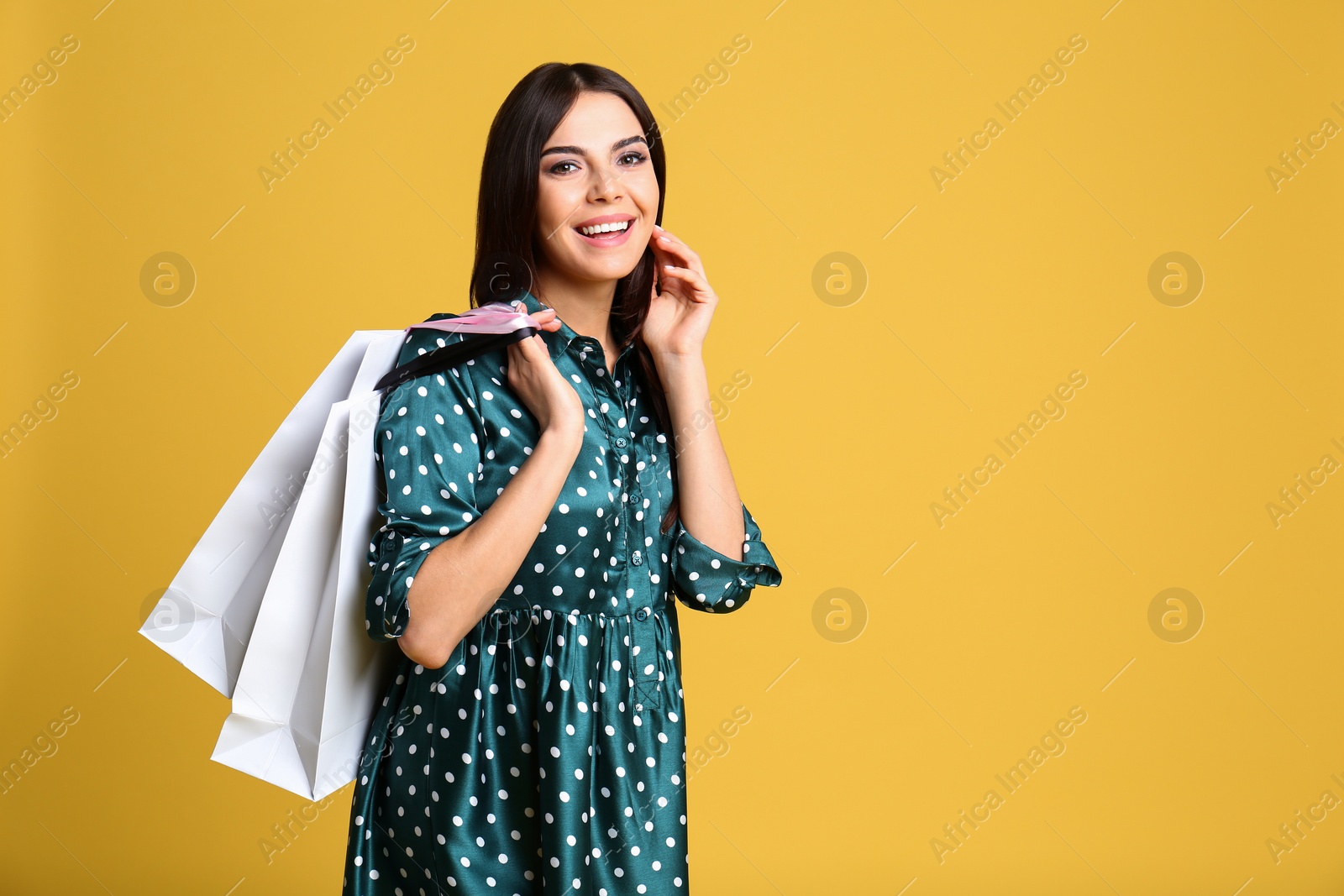 Photo of Portrait of young woman with paper bags on yellow background, space for text