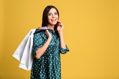 Photo of Portrait of young woman with paper bags on yellow background, space for text