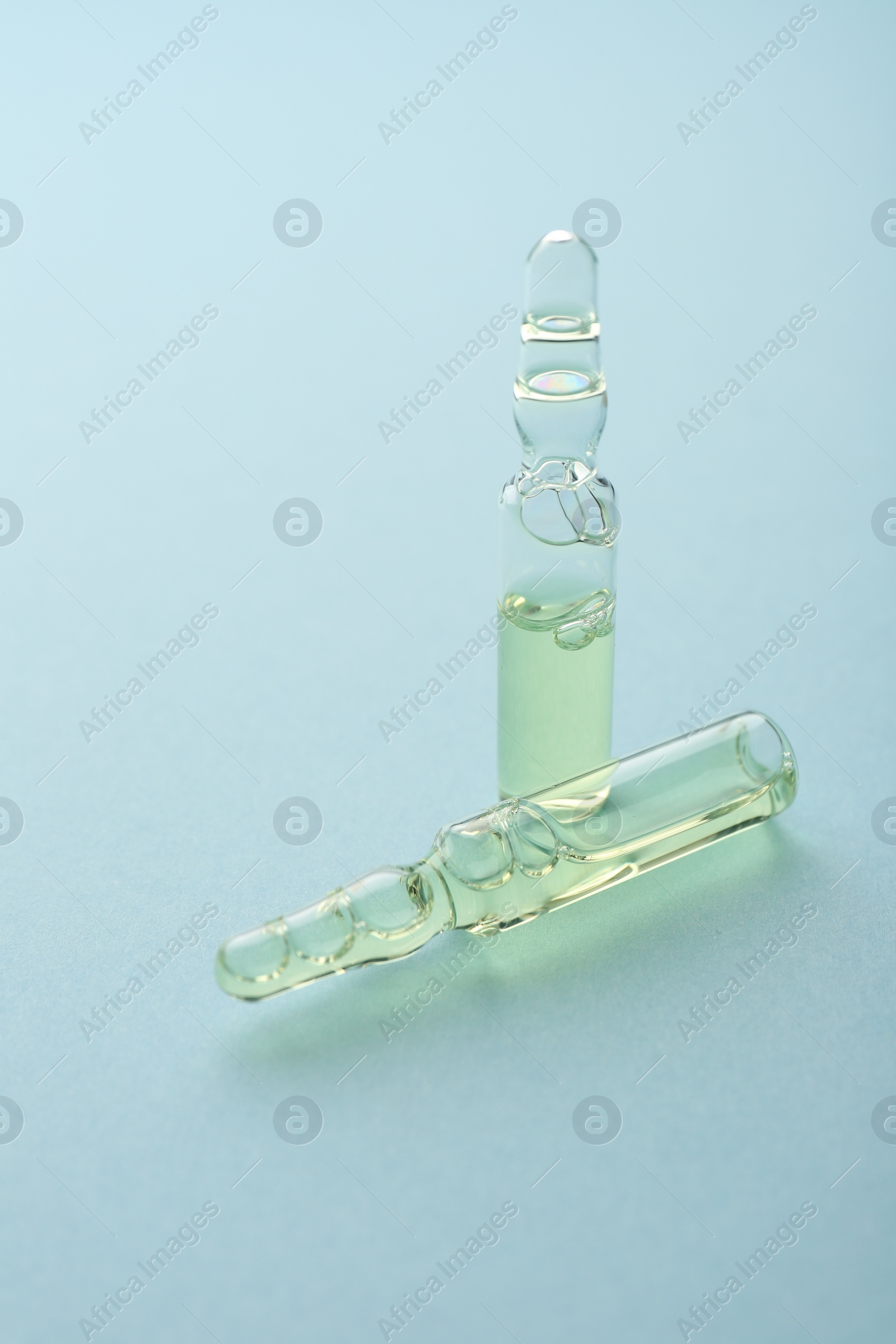 Photo of Glass ampoules with liquid on light blue background