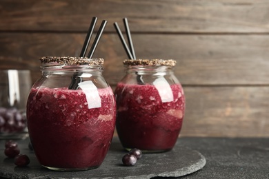 Photo of Jars of delicious acai juice with cocktail straws on dark table against wooden background