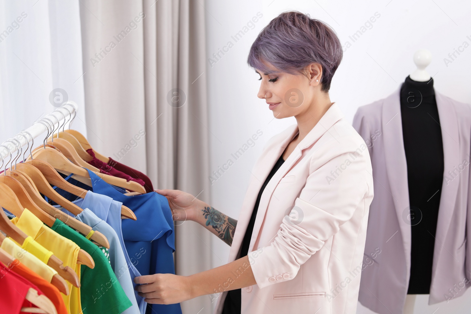 Photo of Beautiful young stylist choosing trendy clothes from rack in studio