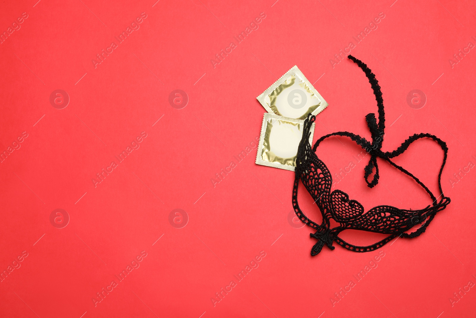 Photo of Lace mask and condoms on red background, top view with space for text. Sex game