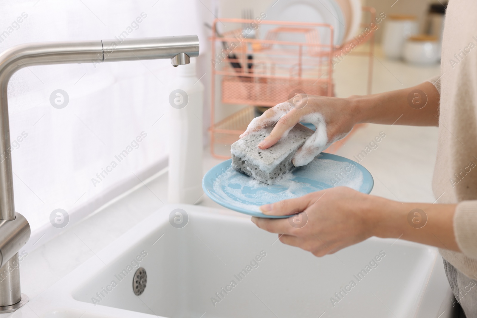 Photo of Woman washing plate above sink in modern kitchen, closeup