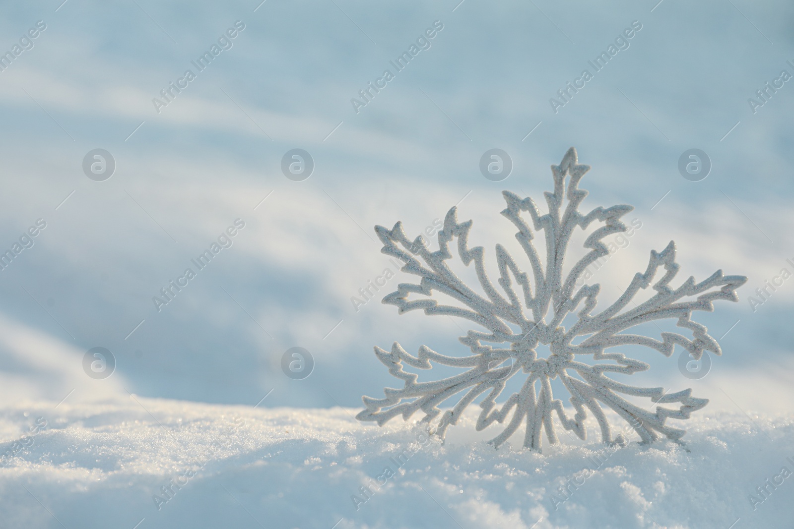 Photo of Beautiful decorative snowflake in white snow, outdoors. Space for text