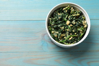 Photo of Tasty spinach dip with egg in bowl on light blue wooden table, top view. Space for text