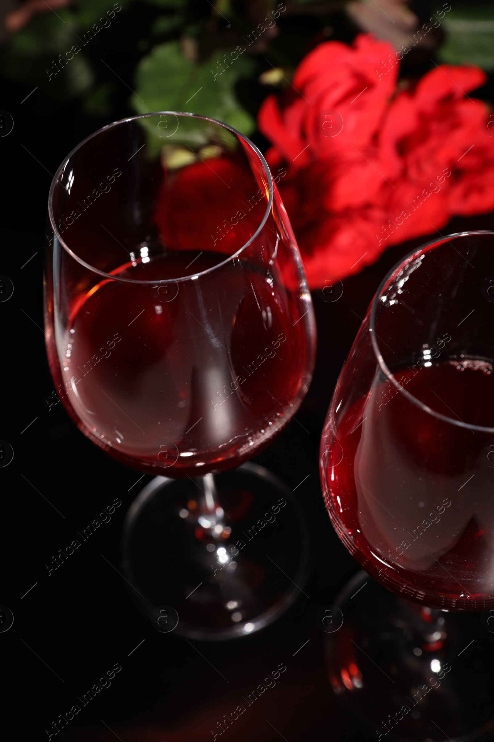 Photo of Glasses of wine and roses for romantic dinner on black table, closeup