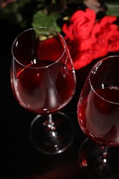 Photo of Glasses of wine and roses for romantic dinner on black table, closeup