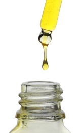 Photo of Dripping yellow facial serum from pipette into glass bottle on white background, closeup