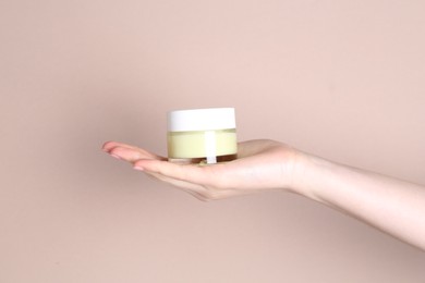 Woman with jar of cream on beige background, closeup