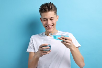 Young man using mouthwash on light blue background