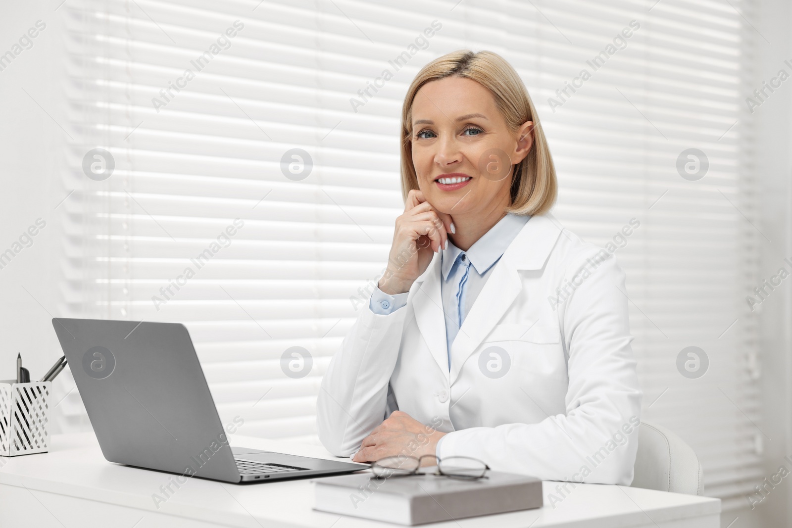 Photo of Portrait of happy dermatologist at white table in clinic