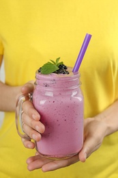 Young woman holding mason jar of tasty blackberry smoothie, closeup