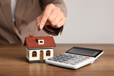 Photo of Mortgage concept. Woman putting coin into house model at wooden table, closeup with space for text