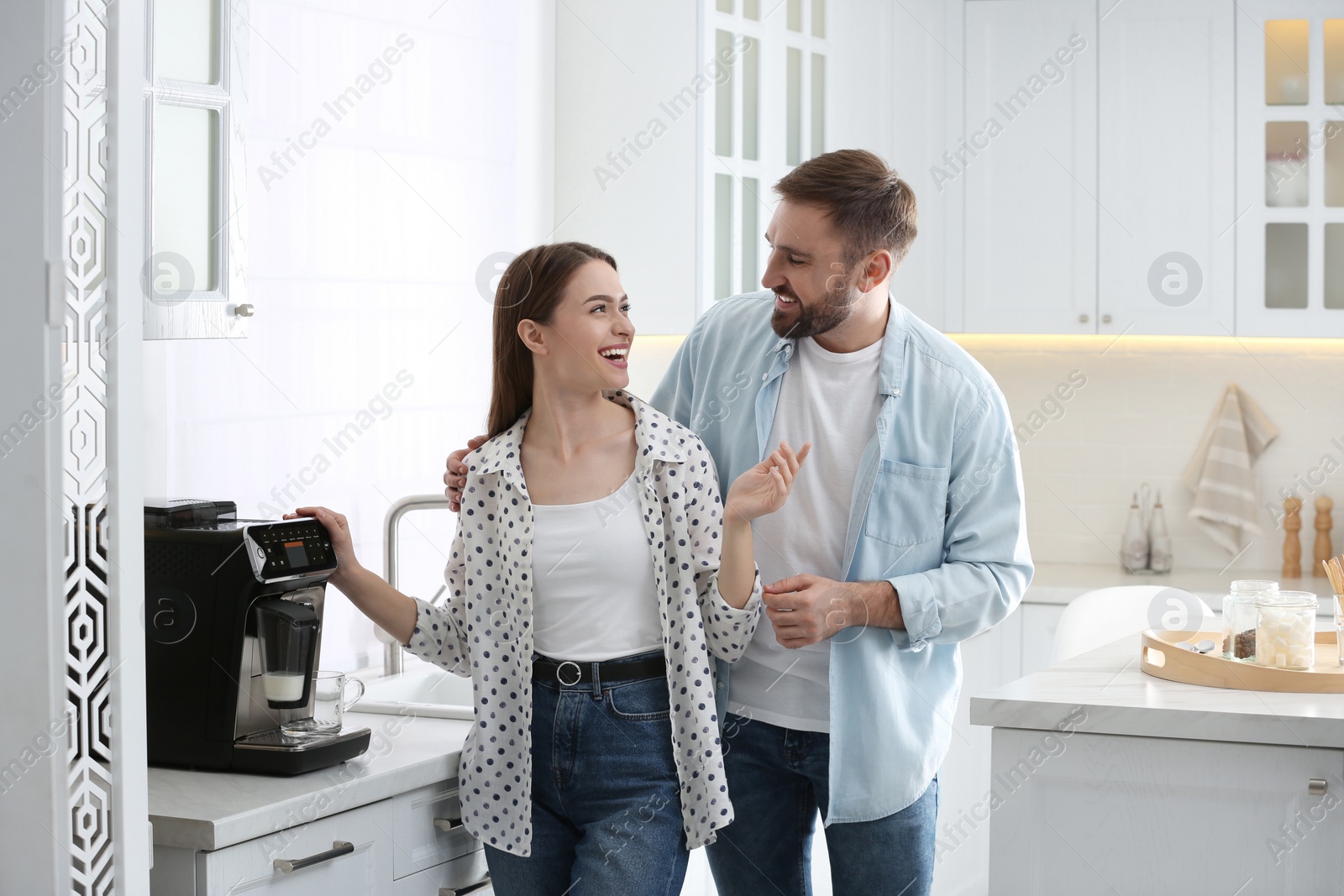 Photo of Happy couple preparing fresh aromatic coffee with modern machine in kitchen