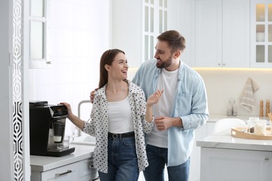 Happy couple preparing fresh aromatic coffee with modern machine in kitchen