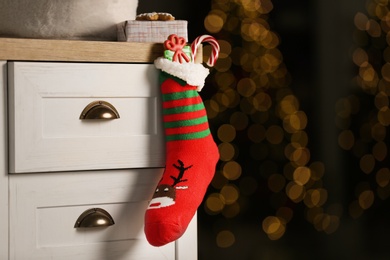 Photo of Stocking with presents hanging on drawer in children's room, space for text. Saint Nicholas Day tradition