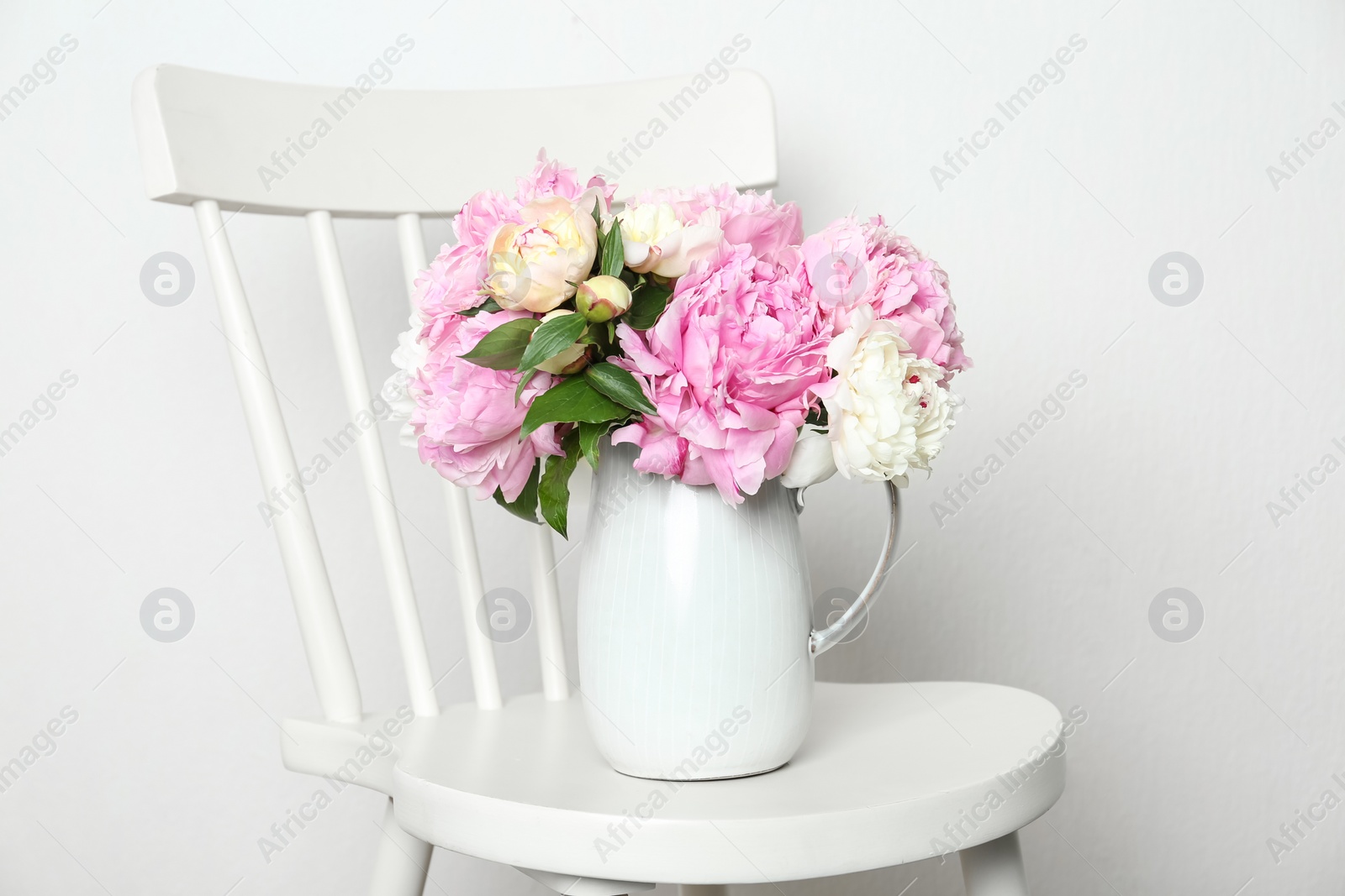 Photo of Beautiful fragrant peonies in jug on white chair