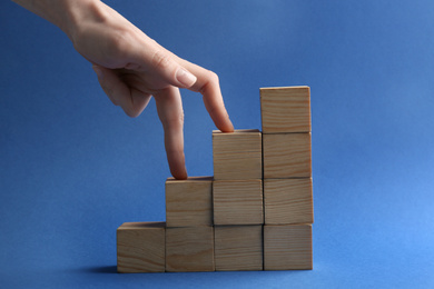 Woman and stairs built with wooden cubes on blue background, closeup. Career promotion concept