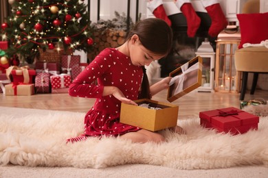Photo of Cute child opening Christmas gift on floor at home