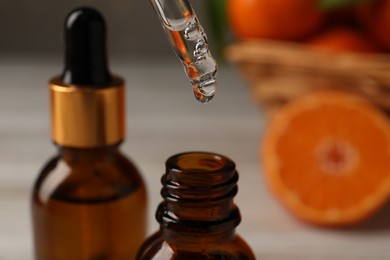 Photo of Tangerine essential oil dripping from pipette into bottle on blurred background, closeup