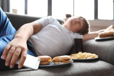 Photo of Overweight boy sleeping on sofa surrounded by fast food