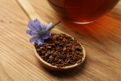 Photo of Spoon of chicory granules with flower on wooden table, closeup