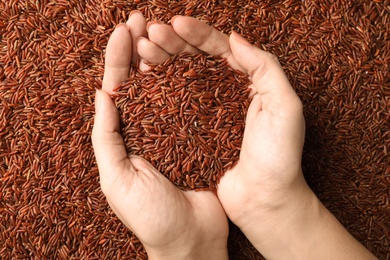 Photo of Woman holding heap of cereal over raw brown rice