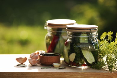 Photo of Jars of delicious pickled cucumbers and ingredients on wooden table against blurred background, closeup. Space for text