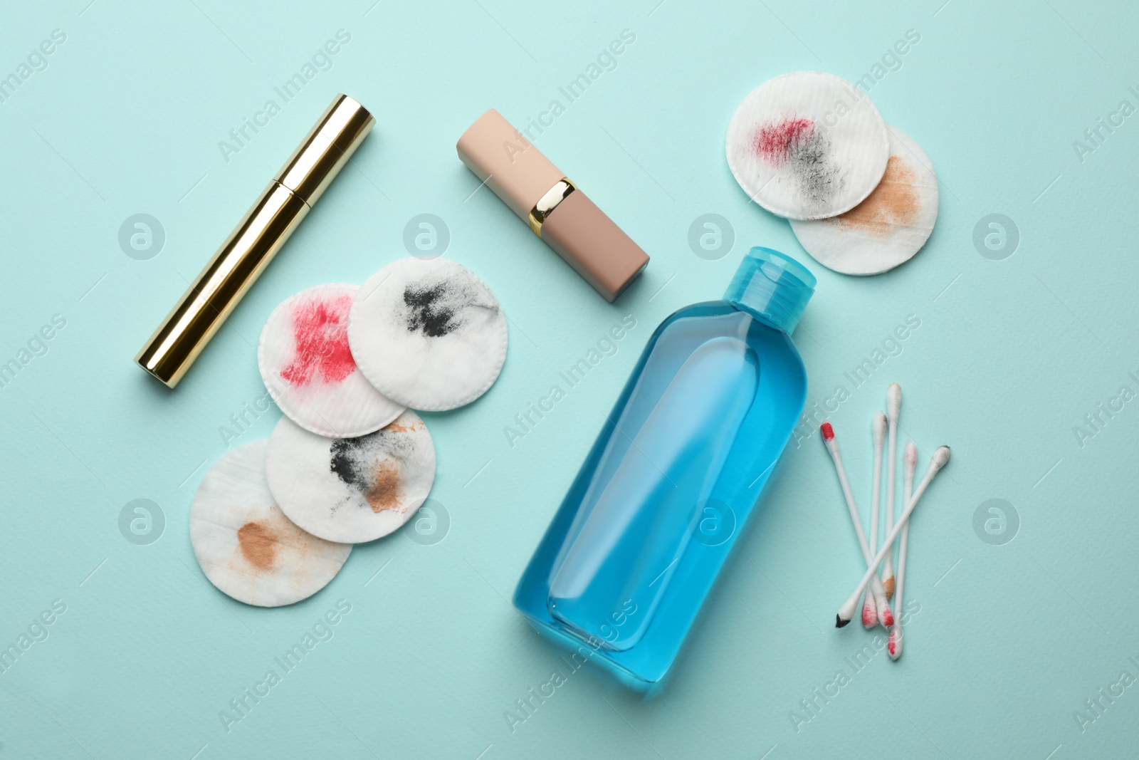 Photo of Dirty cotton pads, swabs, cosmetics and makeup removal product on light blue background, flat lay