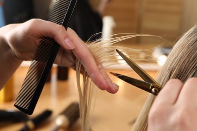 Hairdresser cutting client's hair with scissors in salon, closeup