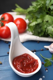 Organic ketchup in spoon and spices on blue wooden table, closeup. Tomato sauce