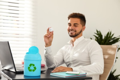 Photo of Young man throwing paper into mini recycling bin at table in office