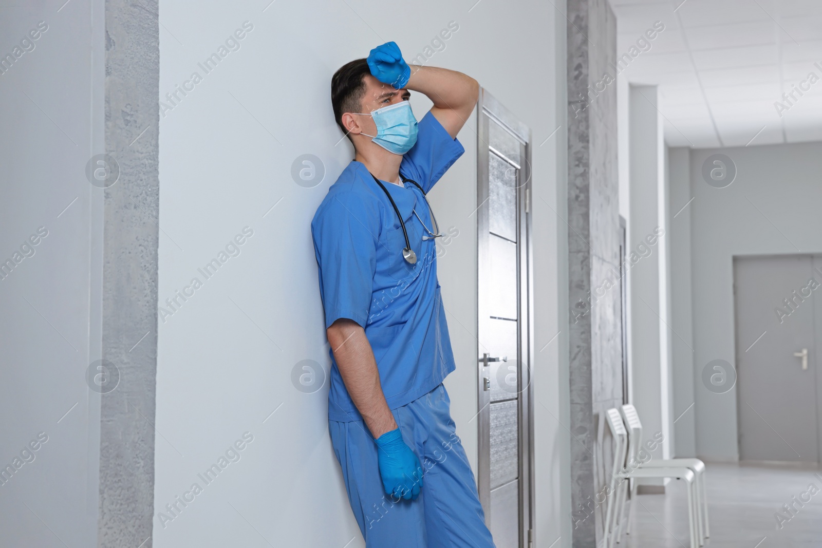 Photo of Exhausted doctor near grey wall in hospital hallway