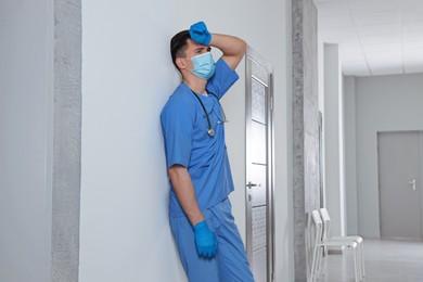 Photo of Exhausted doctor near grey wall in hospital hallway