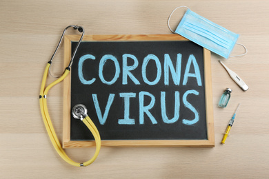 Photo of Chalkboard with words CORONA VIRUS and stethoscope on wooden background, flat lay