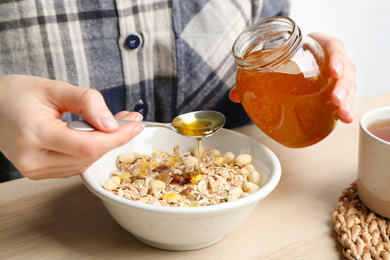 Photo of Woman putting honey into bowl with muesli at wooden table, closeup