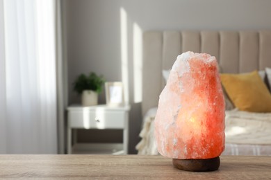 Photo of Beautiful Himalayan salt lamp on wooden table in bedroom, space for text