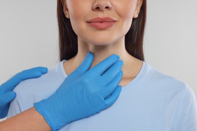 Endocrinologist examining thyroid gland of patient on light grey background, closeup