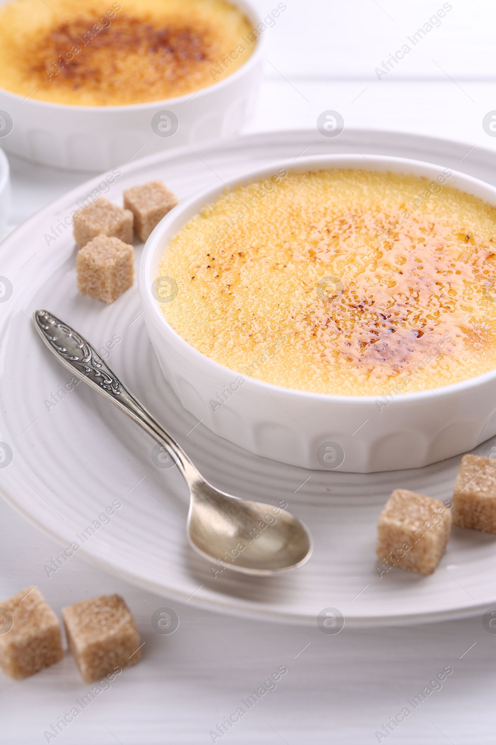 Photo of Delicious creme brulee in bowls, sugar cubes and spoon on white wooden table