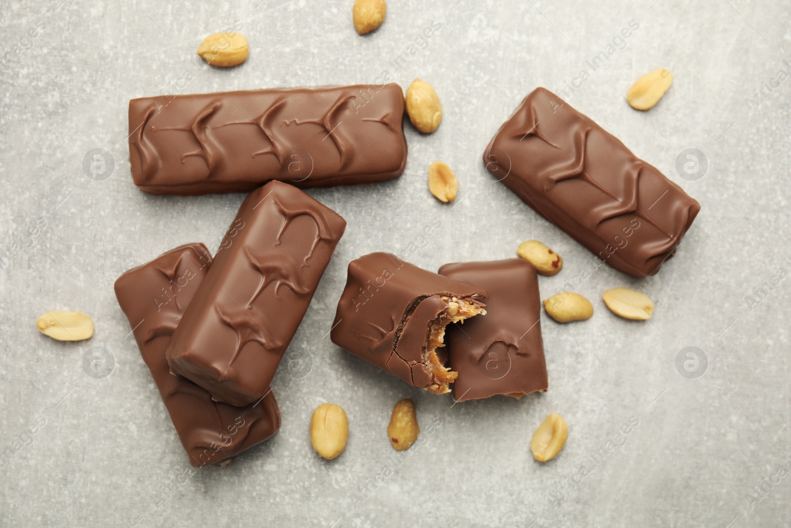 Photo of Chocolate bars with caramel, nuts and nougat on light grey table, flat lay