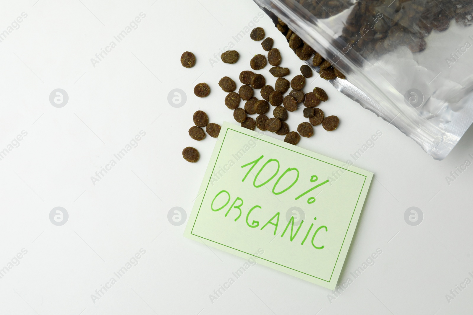 Photo of Overturned pack of dry cat food and note 100% Organic on white table, flat lay. Space for text