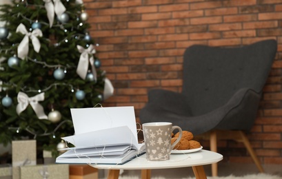 Book with treat on table and Christmas tree in stylish living room interior