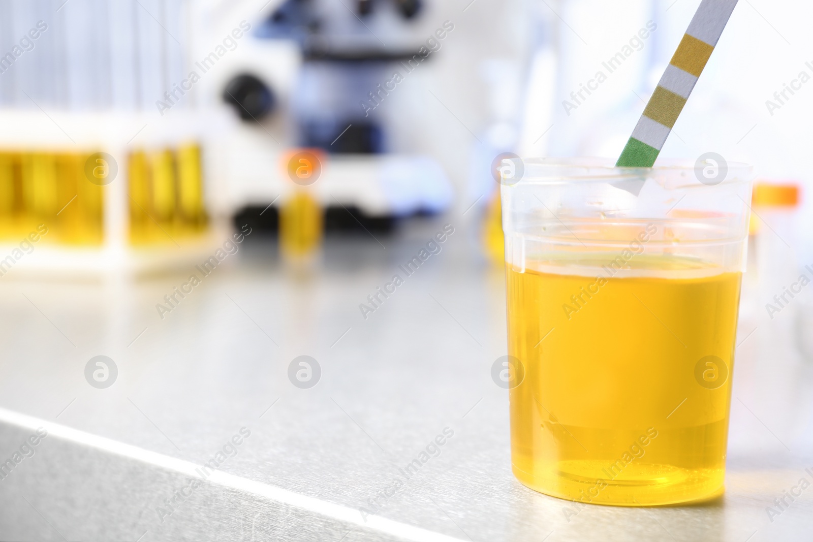 Photo of Putting litmus paper into container with urine sample on table in laboratory, space for text. Medical analysis